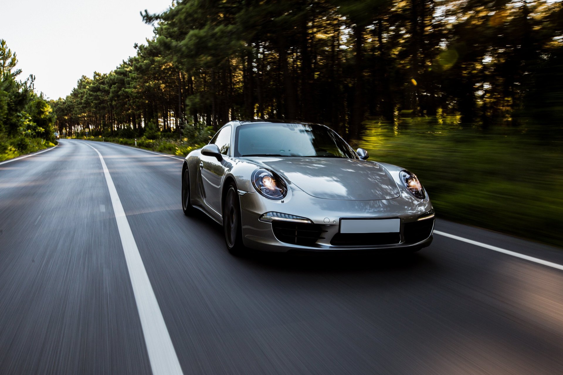 Silver Porsche sports car driving on a tree-lined highway with motion blur effect